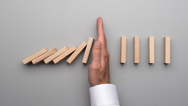 Kippende Dominosteine und helfende Hand.
